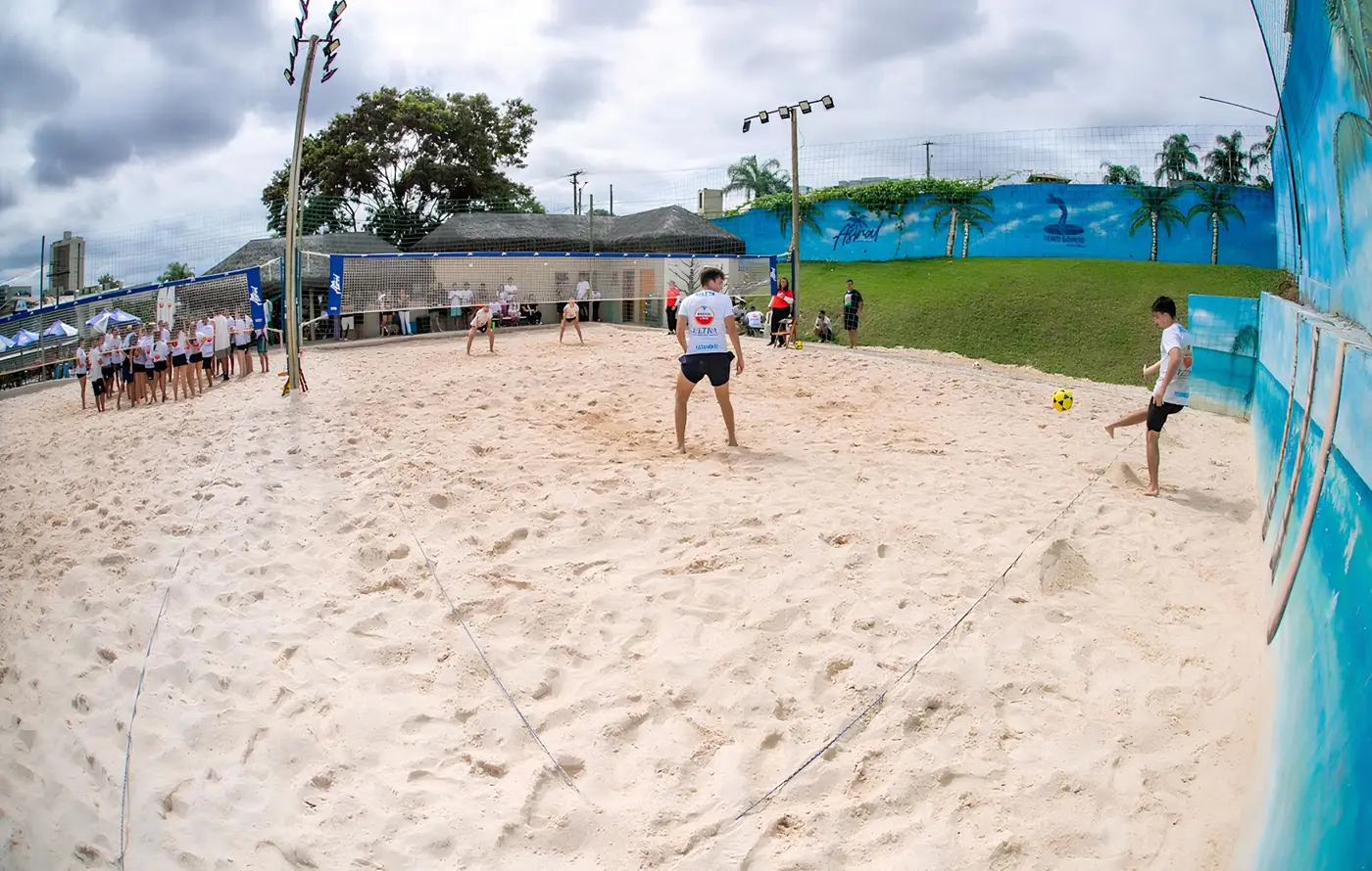 Quadra de areia de uma arena parceira cheia, com jogo em andamento e público durante um evento
